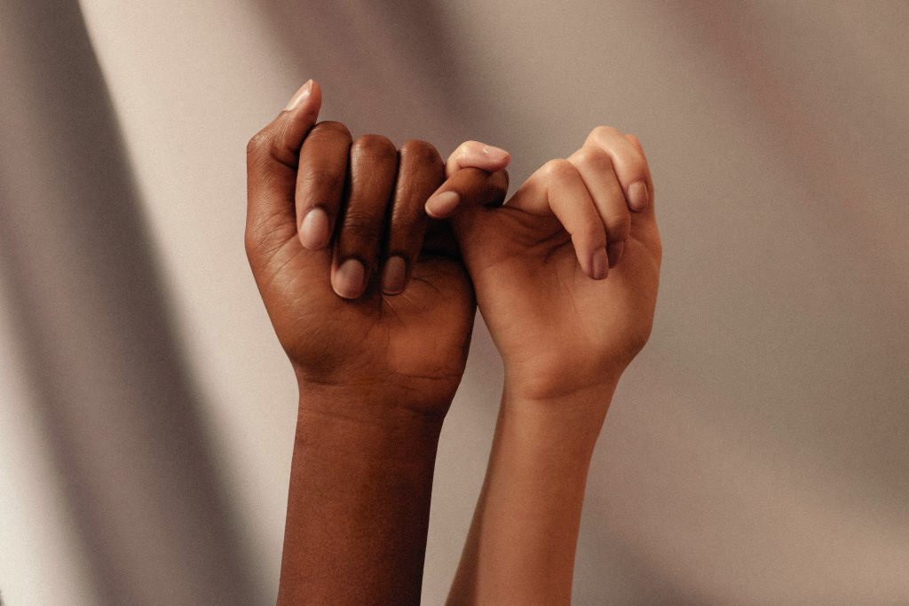 Hands of two women with different skin tones against a neutral background