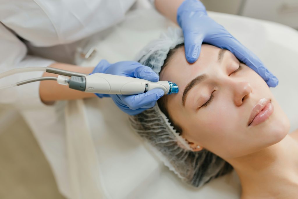 woman laying down with eyes closed with another person treating her skin with a laser